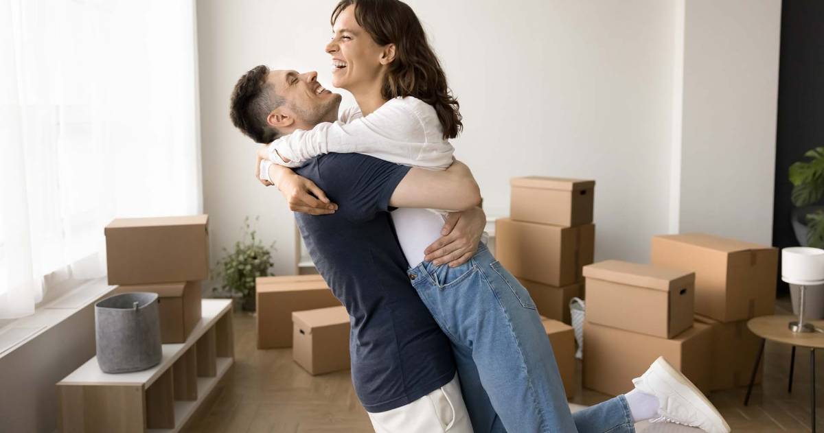 Eerste woning een droom die uitkomt jongen tilt een vrouw op in een woonkamer met allemaal dozen